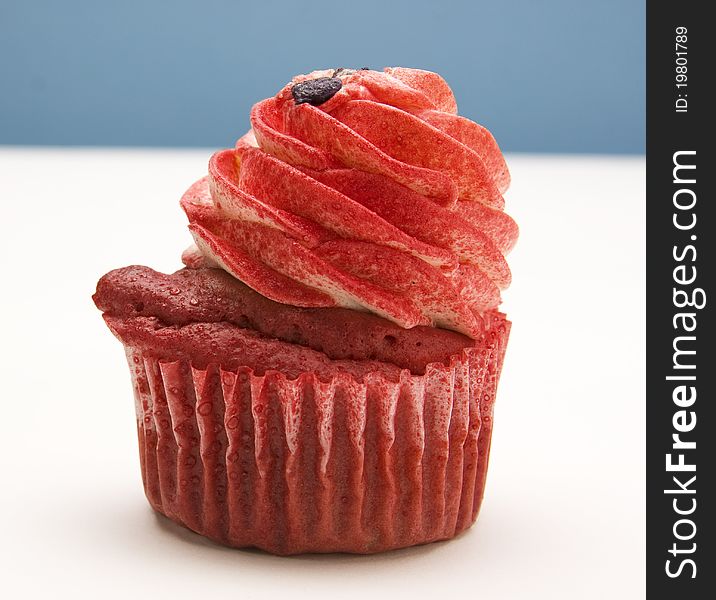 Red velvet cupcake decorated with red colored buttercream frosting against a blue and white background.