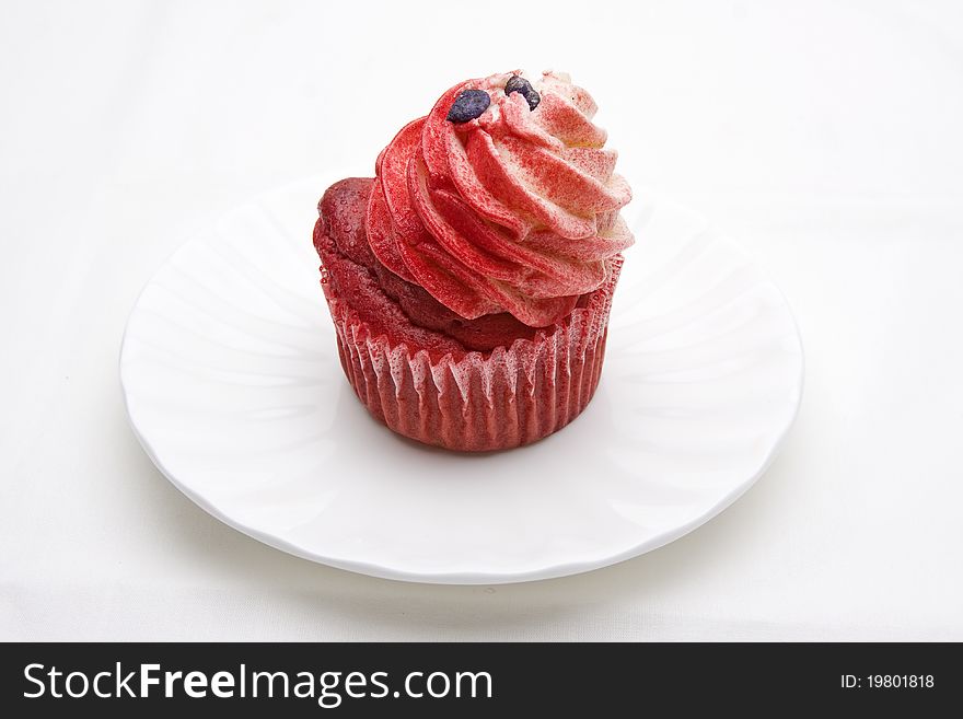 Red velvet cupcake decorated with red colored buttercream frosting on a white plate against a white background.