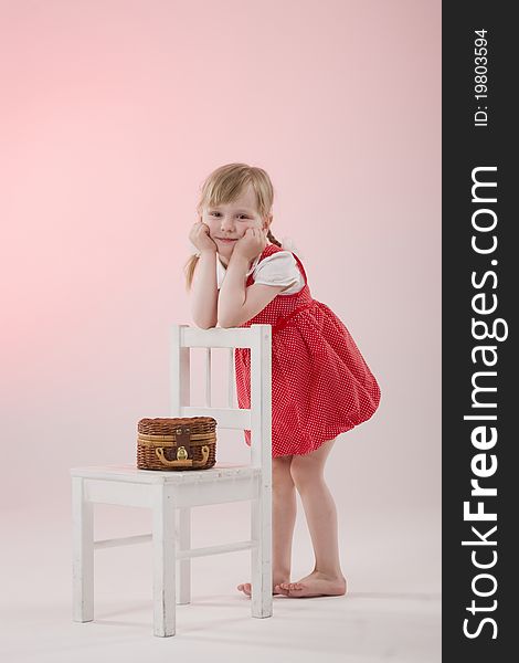 Girl in red dress with wicker and pigtails near chair. Girl in red dress with wicker and pigtails near chair