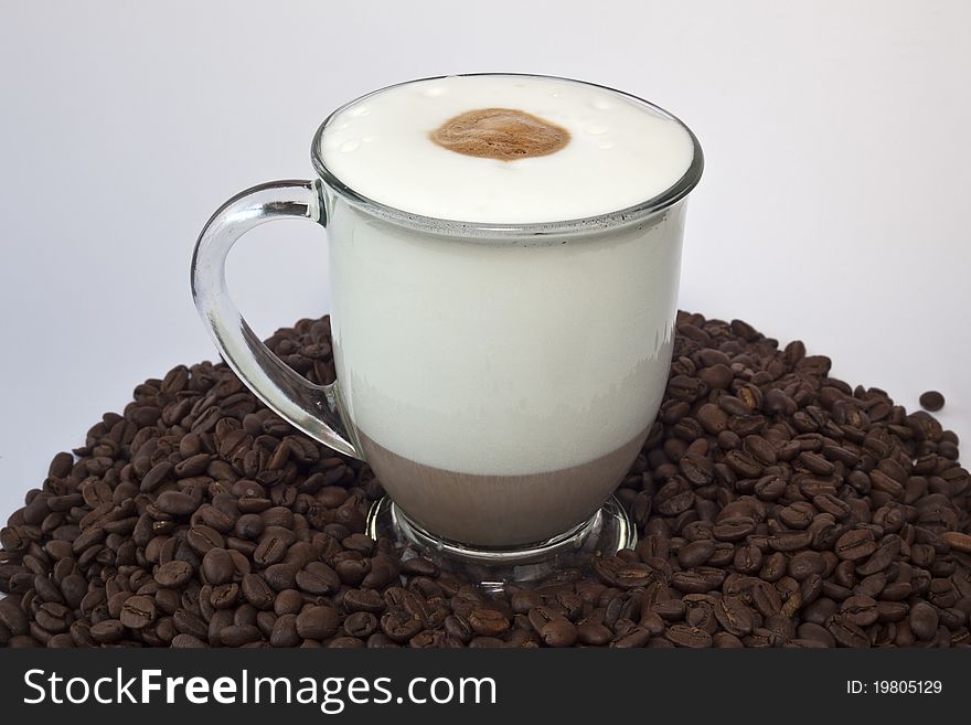 Cappuccino in a large mug on pile of beans with white background