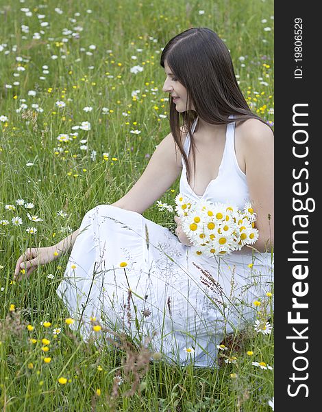 Beautiful girl in a white dress sitting in a flowery meadow and picking flowers (daisies). Beautiful girl in a white dress sitting in a flowery meadow and picking flowers (daisies)