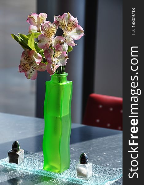 A flower arrangement in a green vase on a table with salt and pepper shakers tasefully decorated for lunch or dinner. A flower arrangement in a green vase on a table with salt and pepper shakers tasefully decorated for lunch or dinner.