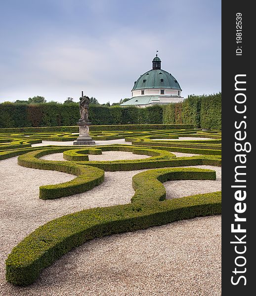 Formal garden of ornamental shaped plants with a statue and historical building in the background; UNESCO side, Kromeriz, The Czech Republic