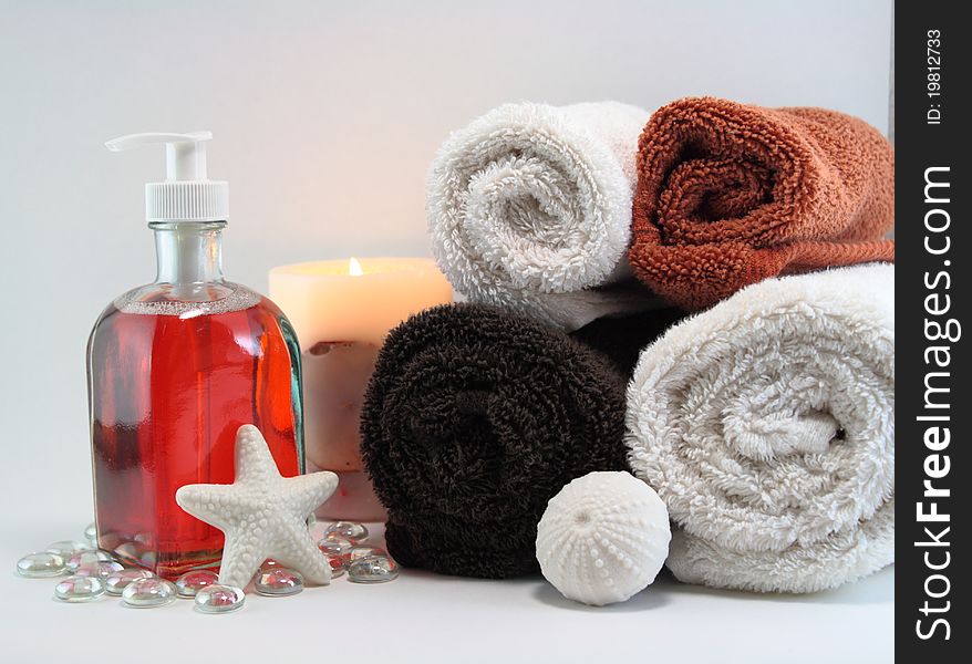 White and colored towels with orange liquid soap, lit candle, and white solid soaps in shapes. White and colored towels with orange liquid soap, lit candle, and white solid soaps in shapes