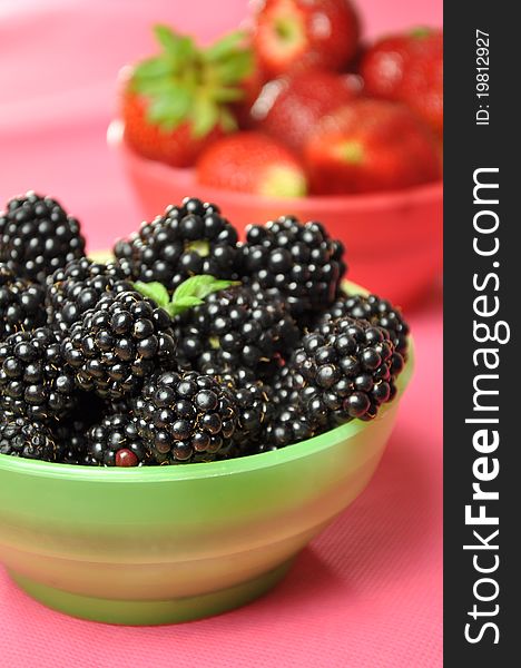 Blackberries and strawberries in colorful bowls on a pink background.