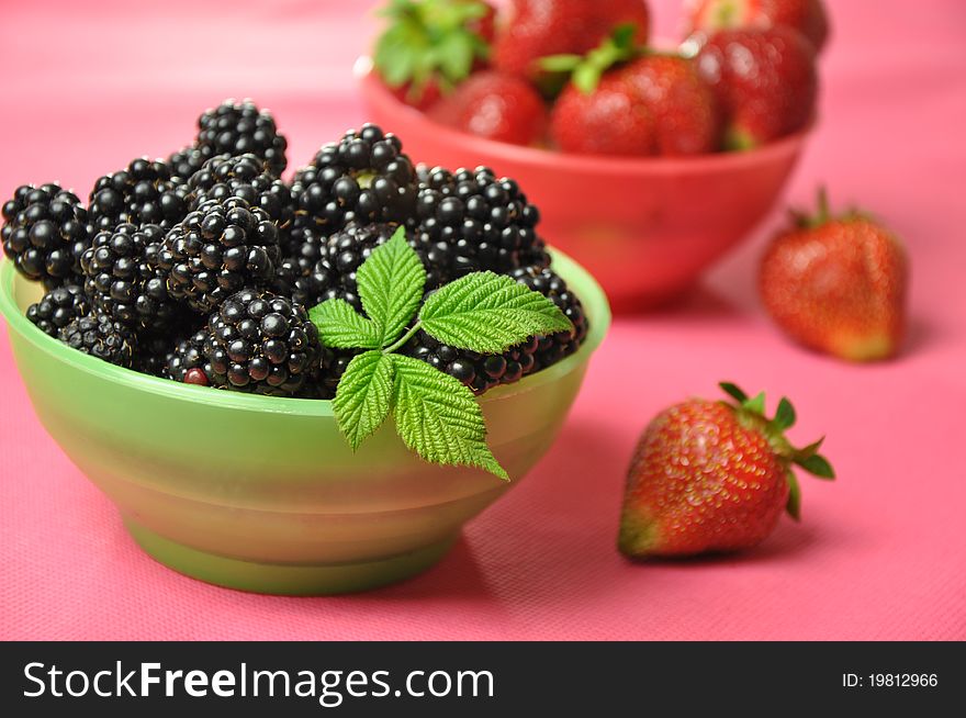 Blackberries and strawberries in colorful bowls on a pink background.