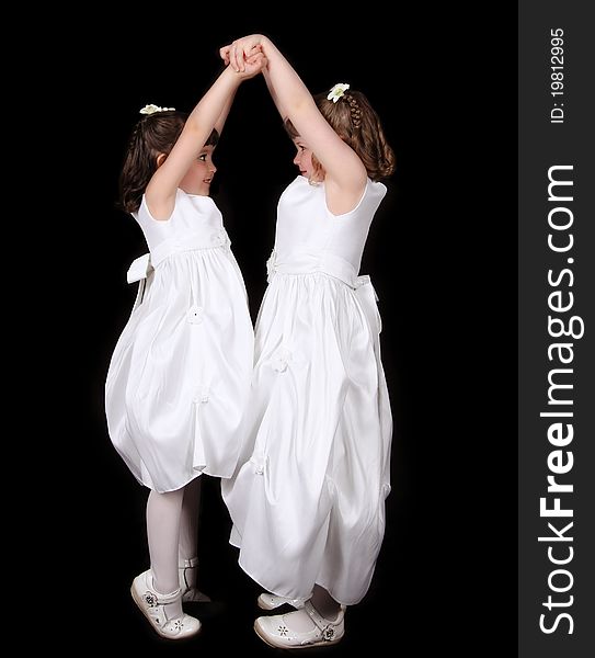 Playful twins in white gowns with hands joined in the air. isolated on black. Playful twins in white gowns with hands joined in the air. isolated on black