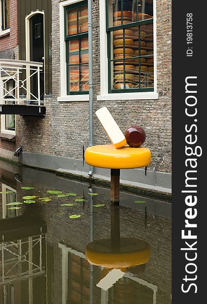 Sculpture of Gouda cheese in a canal besides a little cheese factory in Gouda (NL). The window displays several Gouda cheeses on the shelfes where they are maturing before they are ready to consume