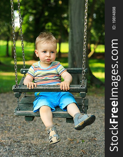 A handsome little boy swinging at the playground in the park