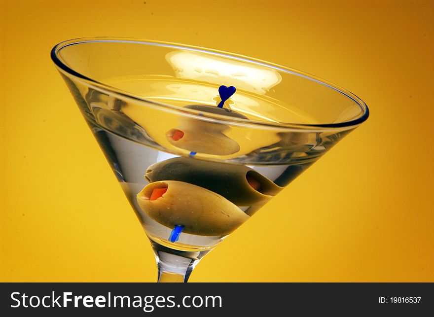 Close up of martini with olive on yellow background