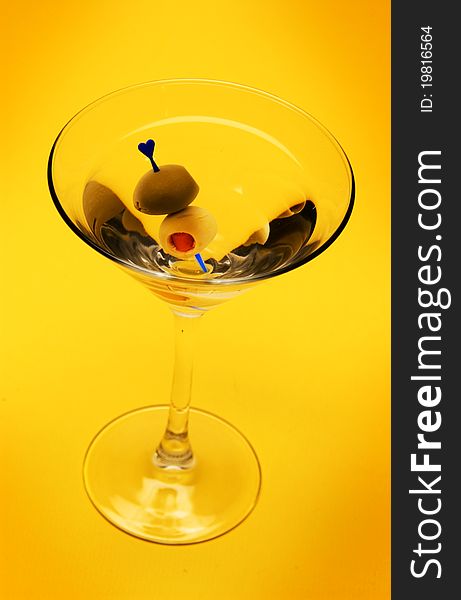Martini with olive on yellow background
