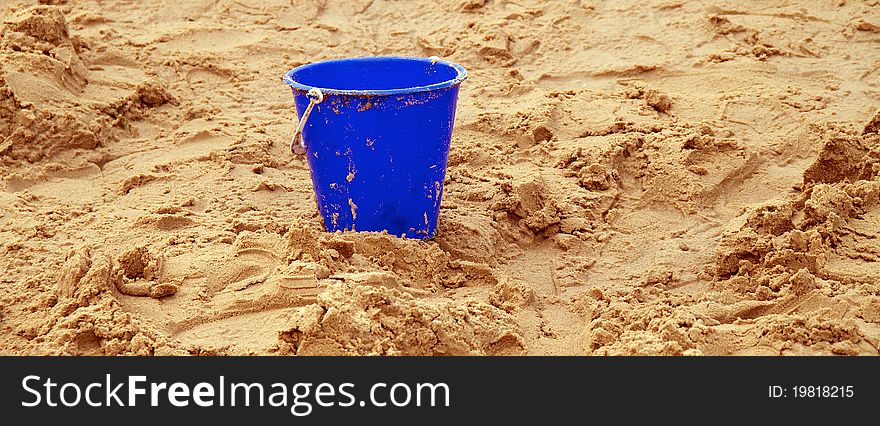 A blue childs bucket upright on sand. A blue childs bucket upright on sand