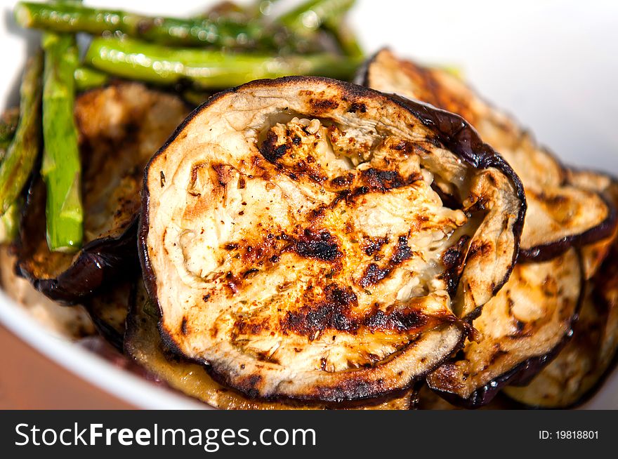 Grilled eggplants and asparagus in a white bowl.