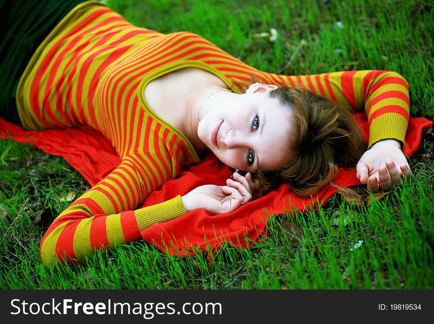Portrait of a girl in a bright colored striped sweater lying on the grass. Portrait of a girl in a bright colored striped sweater lying on the grass