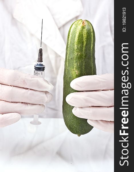 Cucumber and syringe in hands of the inspector on quarantine in a white dressing gown