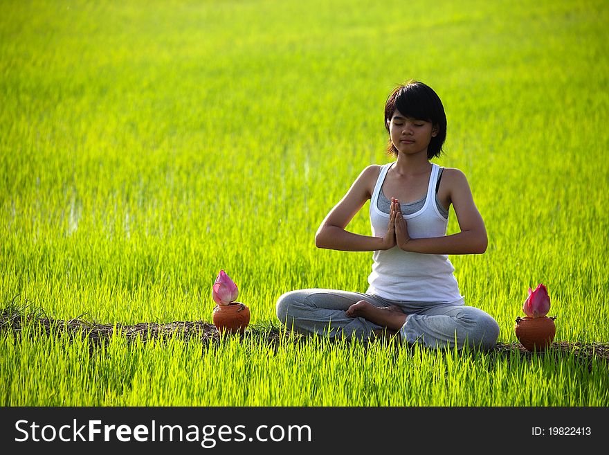 Girl practicing yoga,sitting with lotus flower in paddy field