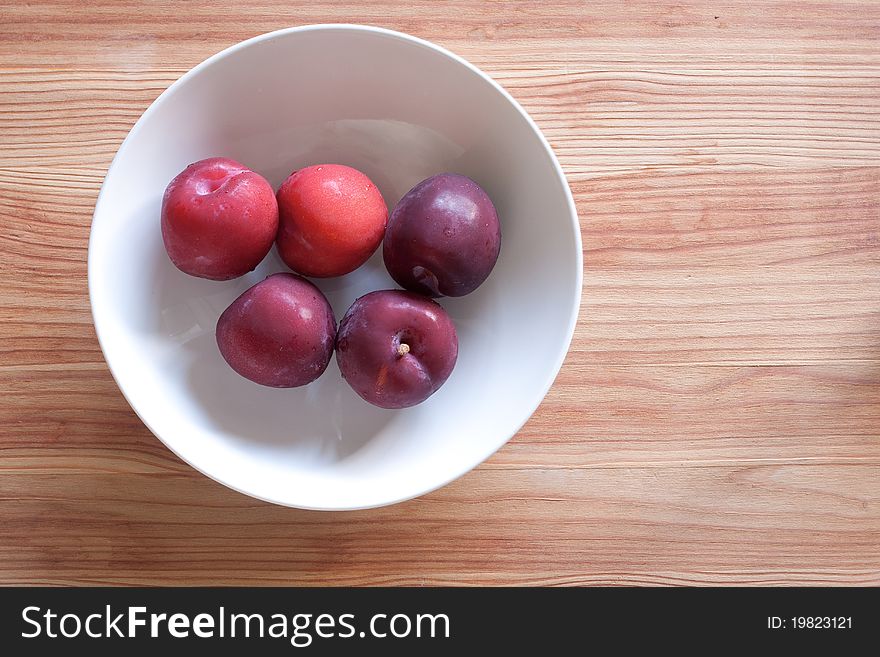 Fresh red plums in a white bowl on a wood board. Fresh red plums in a white bowl on a wood board