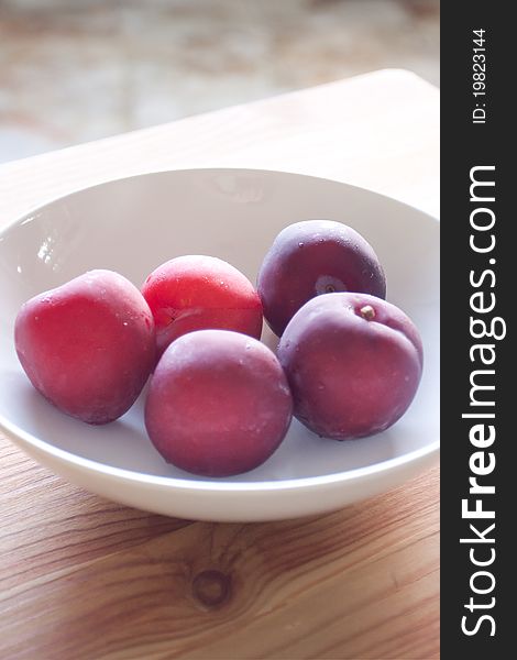 Fresh red plums in a white bowl one a wood board. Fresh red plums in a white bowl one a wood board