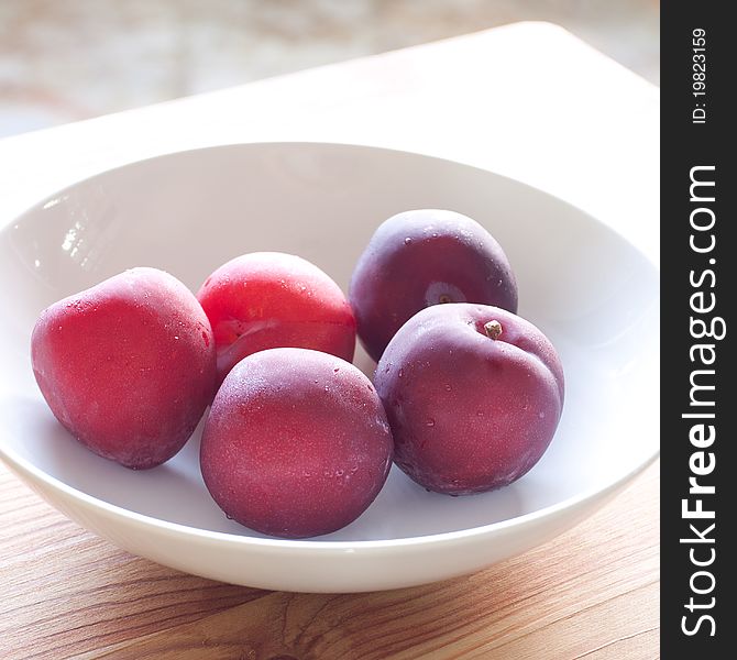 Fresh plums in a white bowl on wood board