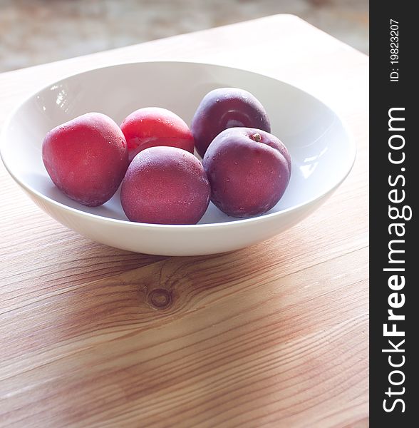 Fresh plums in a white bowl, on wooden board