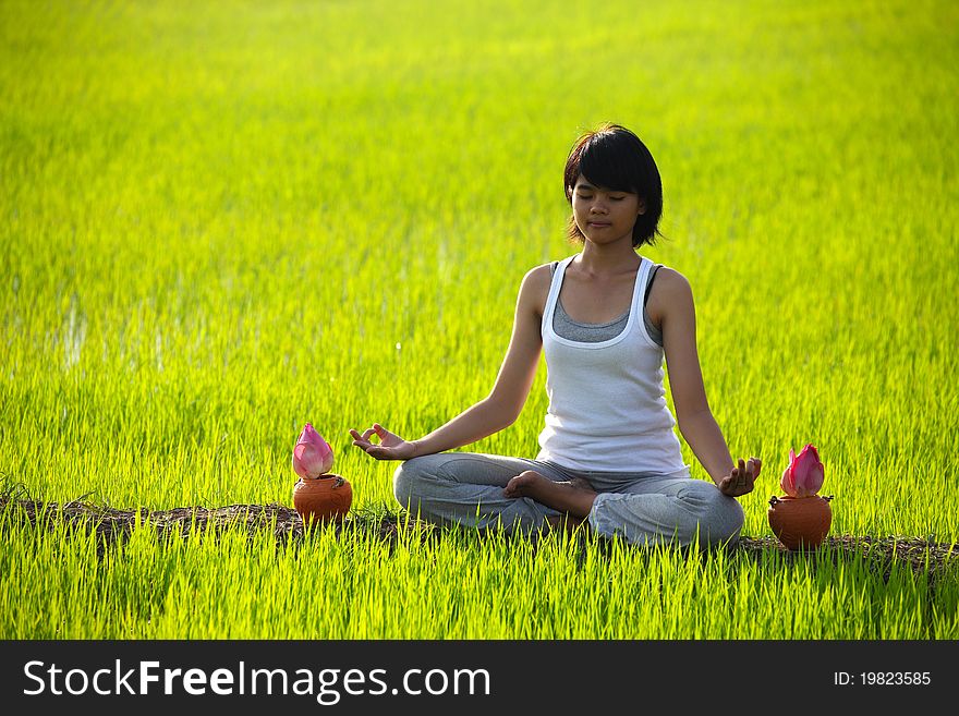 Beautiful girl practicing yoga,sitting with lotus flower in paddy field
