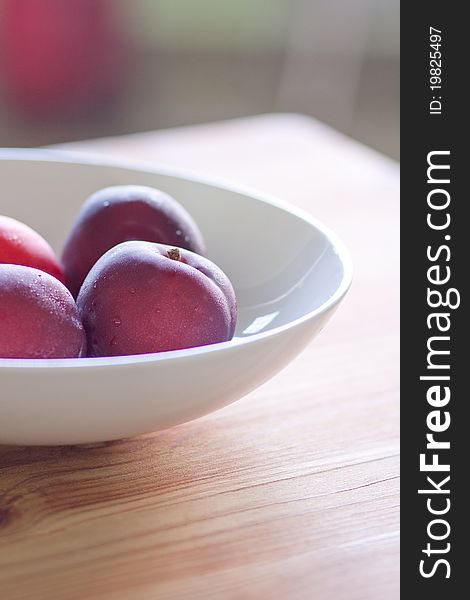 Close up of fresh Plums in a white bowl on a wooden table