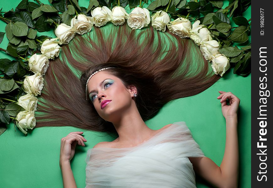 Young girl lay among the flowers of roses on a green background