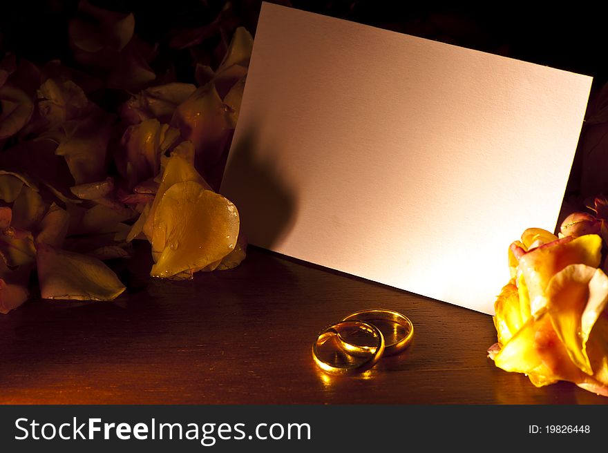 White card with wedding rings, surrounded by rose petals