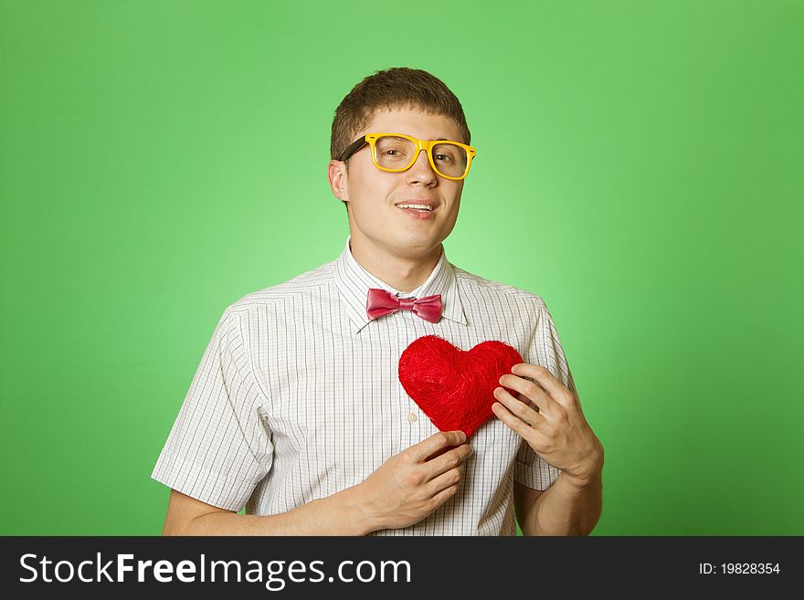 Closeup of young attractive man in a shirt, bow tie and glasses smiling holding a red heart. Closeup of young attractive man in a shirt, bow tie and glasses smiling holding a red heart