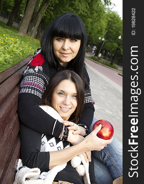 Mother and daughter in a park sitting on a wooden bench eating apples