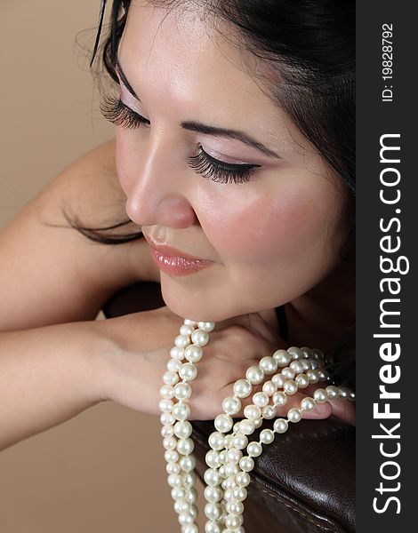Beautiful brunette female leaning on chair back with pearls. Beautiful brunette female leaning on chair back with pearls