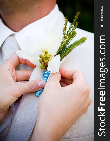 A close up of a bride putting on a boutonniere