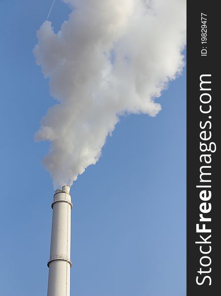 View of smoking smokestack against blue sky