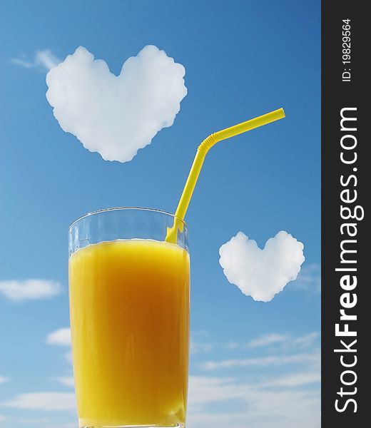 Yellow fruit (orange) juice in glass on a background blue sky. Clouds in the form of hearts. Yellow fruit (orange) juice in glass on a background blue sky. Clouds in the form of hearts.