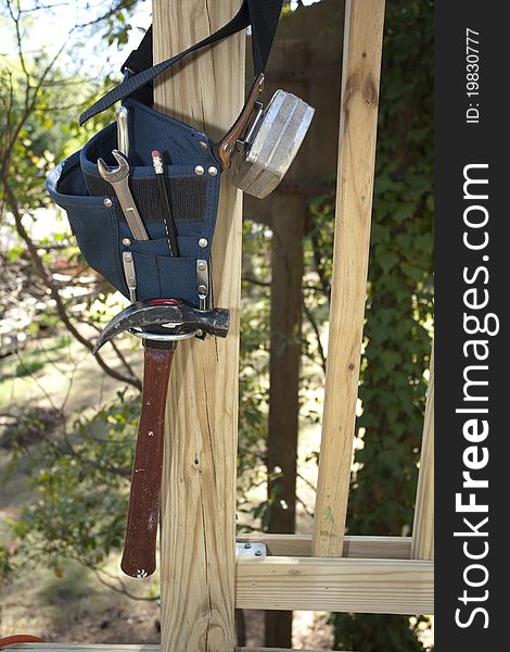 Vertical photograph of a tool belt and tool hanging from a deck railing. Vertical photograph of a tool belt and tool hanging from a deck railing