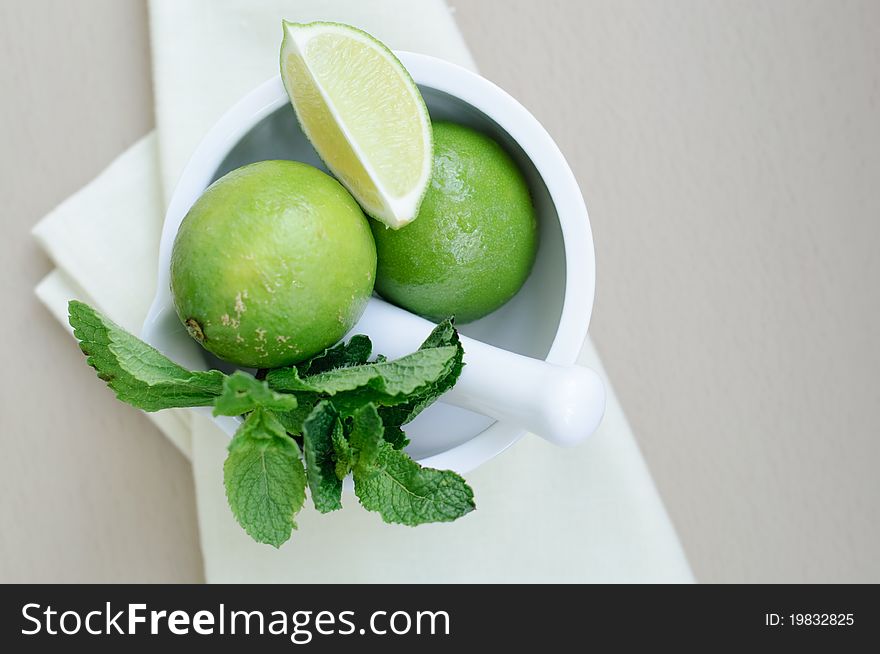 Limes and mint leaves in a white ceramic mortar.