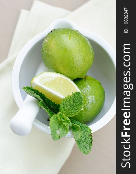 Limes and mint leaves in a white ceramic mortar.