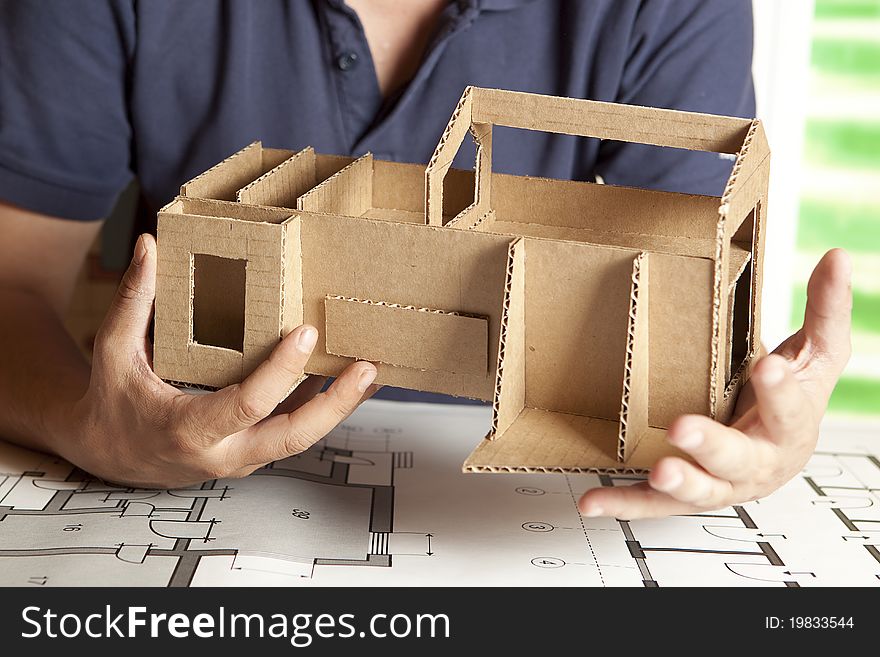 A male architect working on blueprints with a model house