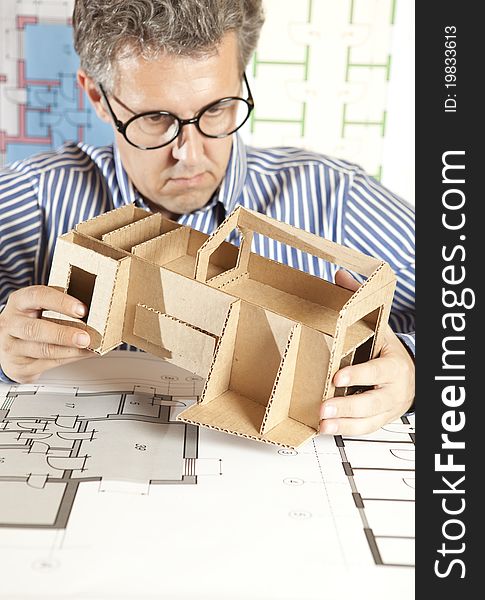 A male architect working on blueprints with a model house