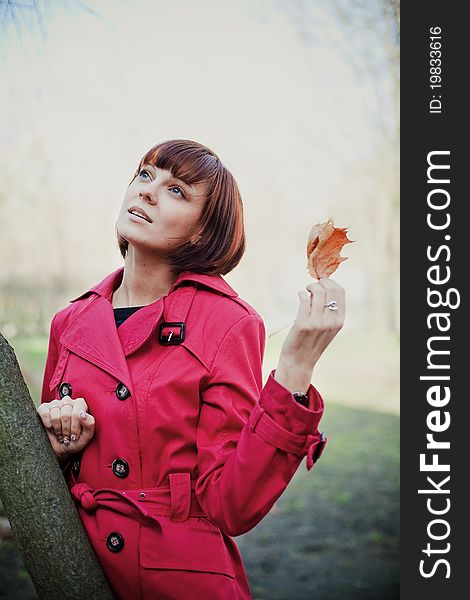 Young beautiful woman in red coat holding orange dry leaf and looking up. Young beautiful woman in red coat holding orange dry leaf and looking up