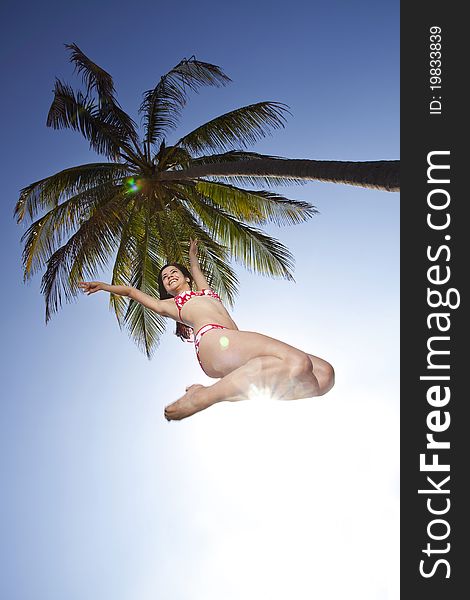Beautiful young woman in bikini smiling and jumping under a palm tree. Beautiful young woman in bikini smiling and jumping under a palm tree