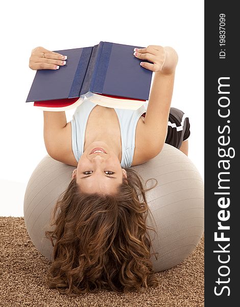 A female laying back on her exercise ball stretching while she reads a book. A female laying back on her exercise ball stretching while she reads a book.