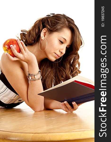 A woman laying on a table reading a good book while eating fruit. A woman laying on a table reading a good book while eating fruit.