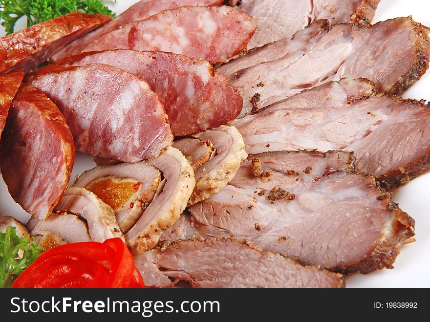 Meat and sausages with parsley and vegetables on white plate. Closeup. Meat and sausages with parsley and vegetables on white plate. Closeup