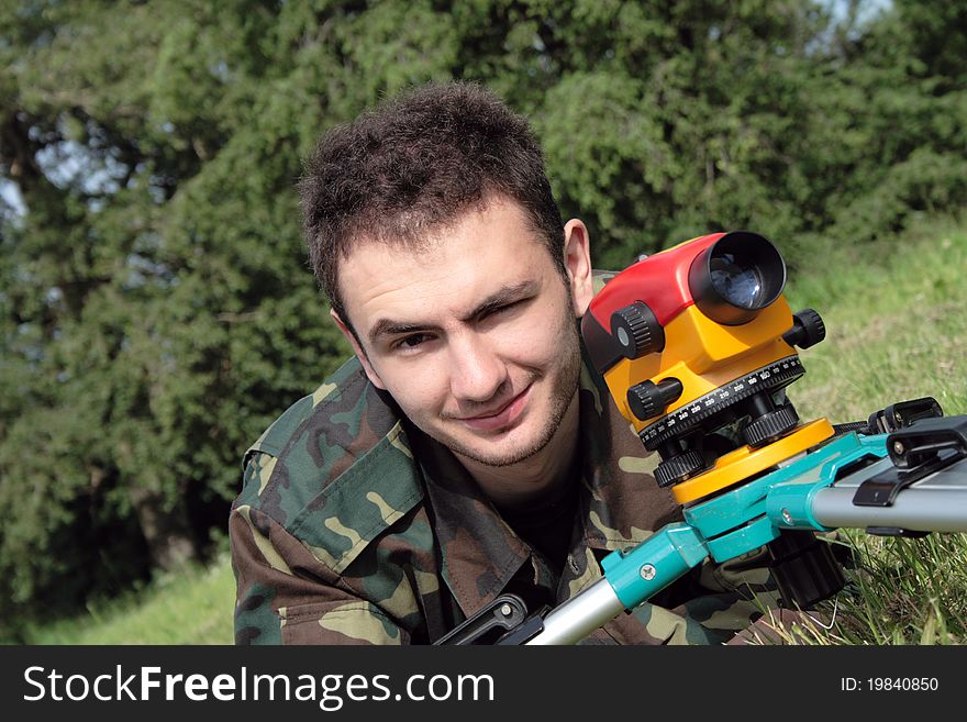 Young man in camouflage with optical instrument