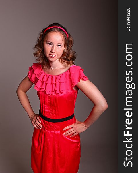 Beautiful woman in beautiful red dress is standing on a dark background in studio. Beautiful woman in beautiful red dress is standing on a dark background in studio.