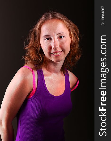 Athletic woman in beautiful purple sporty dress against dark background with part of pink bra. Athletic woman in beautiful purple sporty dress against dark background with part of pink bra.
