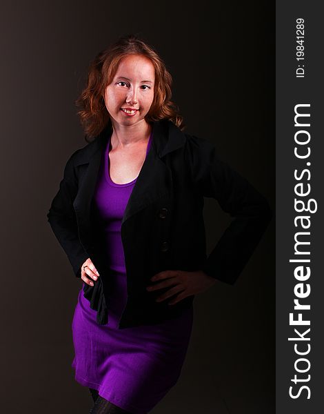 Business woman in beautiful purple sporty dress and a jacket is standing on a dark background. Business woman in beautiful purple sporty dress and a jacket is standing on a dark background.