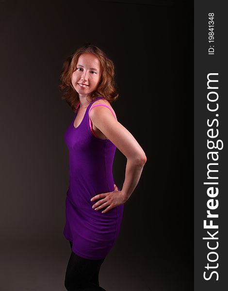 Sweet woman in beautiful purple sporty dress is standing on a dark background. Sweet woman in beautiful purple sporty dress is standing on a dark background