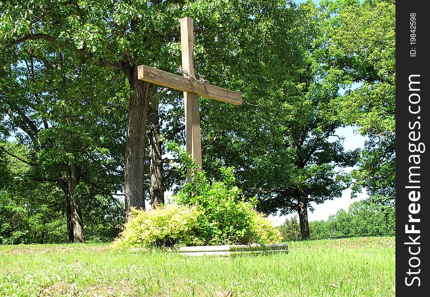 Wooden cross in a churchyard with a crown of thorns surrounded by bushes. Wooden cross in a churchyard with a crown of thorns surrounded by bushes